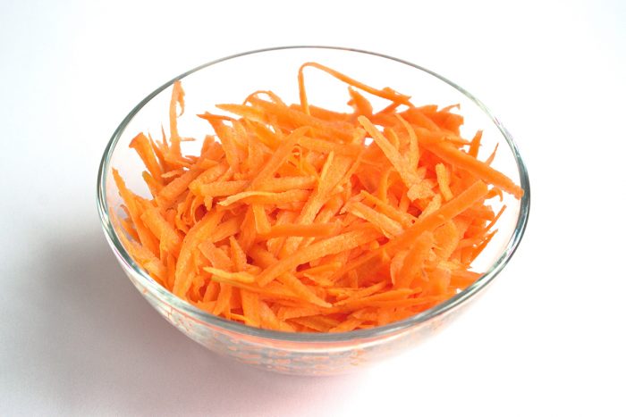 Grated carrots in a bowl on a white background