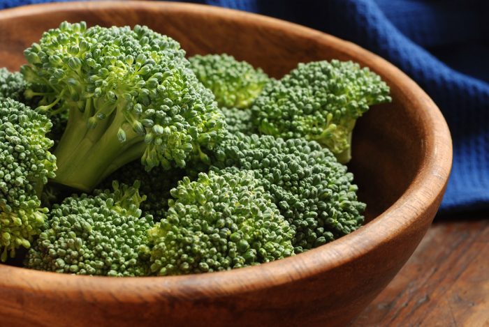 Fresh organic broccoli florets - (uncooked) - in wooden bowl on