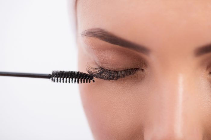 Close-up of young woman applying mascara on her long eyelash by brush